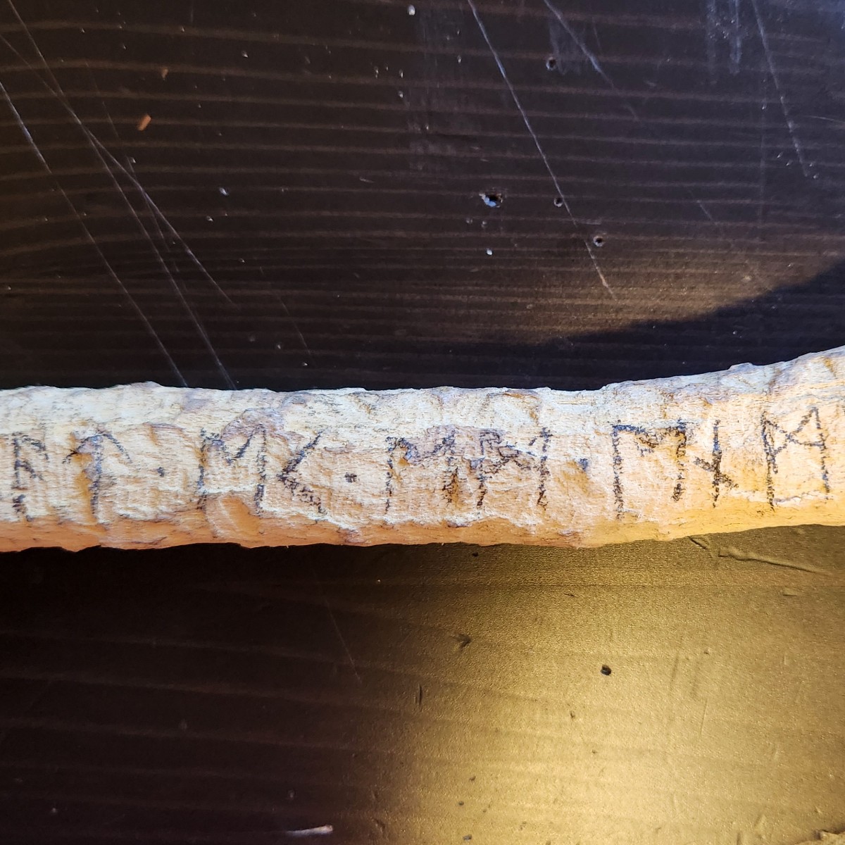 A section of a pale stick with runes drawn in pencil.
