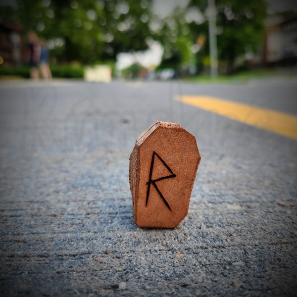 The rune Raidho is burned into a small leather tile, standing on a paved bike path.