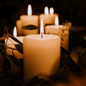Several candles standing on a table, wrapped in winter-seasonal plants.