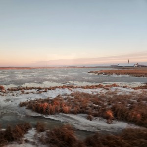 Dakotan landscape with patches of grass and snow at sunrise, seen from a train window.