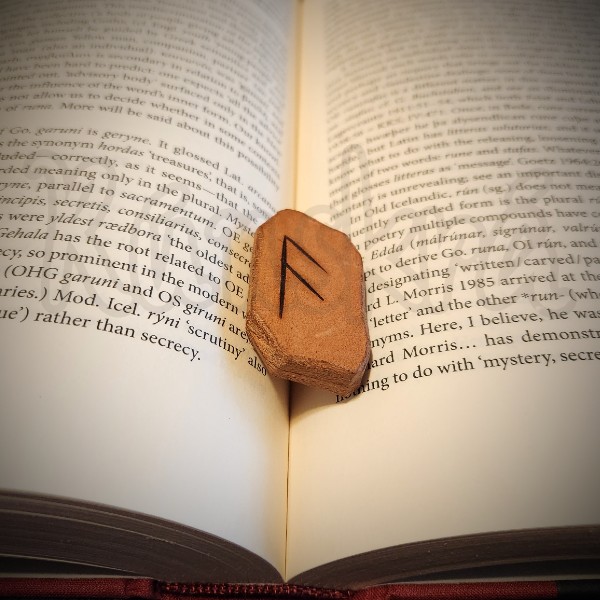 The rune Ansuz, burned into a leather tile, rests between pages on Liberman's Emergence of the Runes.